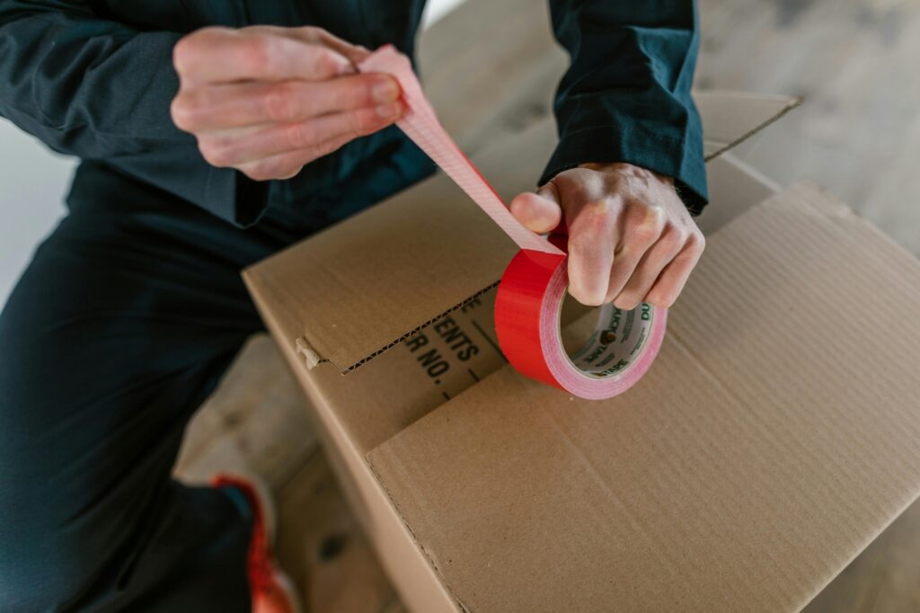A man is sealing a carton with a packing tape.