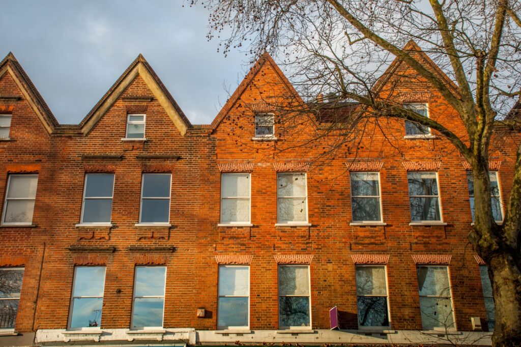 Towering brick townhouses with glass windows and a tall tree in front