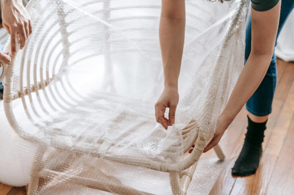 Cropped image of a professional mover wrap a chair with bubble wrap in the concept of 'the benefits of using a professional home removals service in Chiswick'.