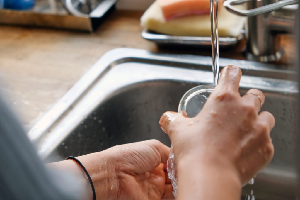 Cropped image of a woman rinsing the glass with running water