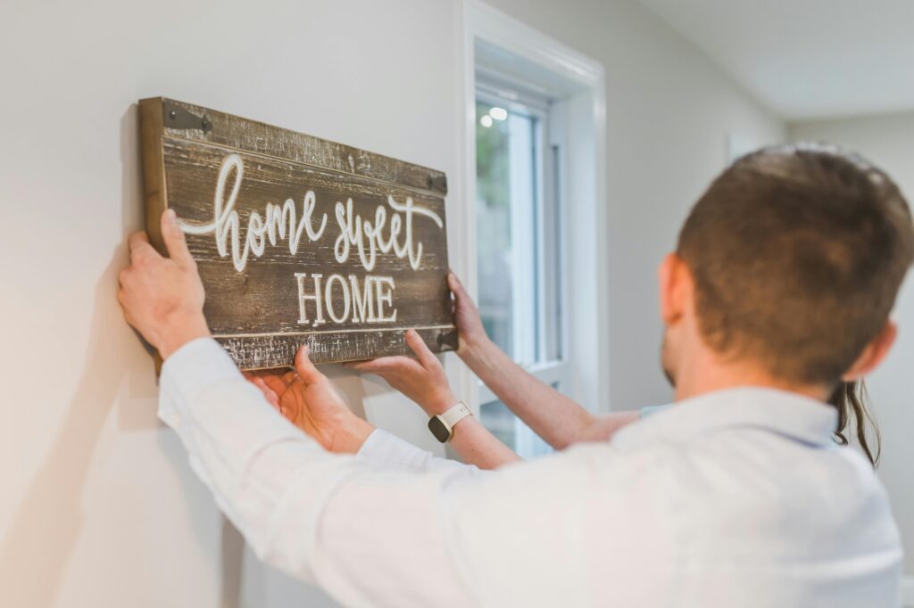 A couple is hanging a 'Home Sweet Home' sign on the wall