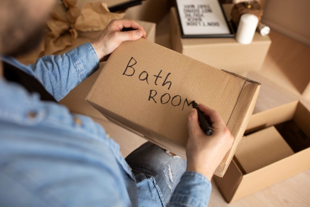 High-angle shot of a man writing the designated room of the moving box